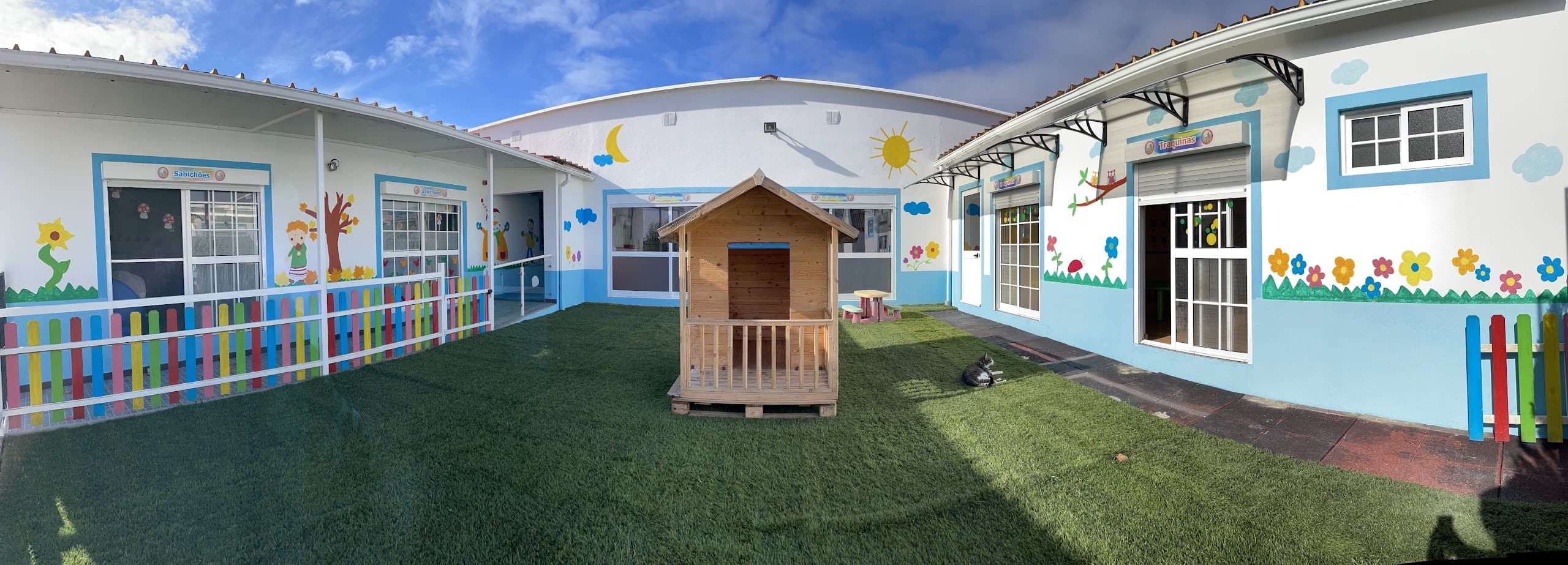 Pátio exterior do Cantinho dos Sonhos, com relvado e casinha de madeira
