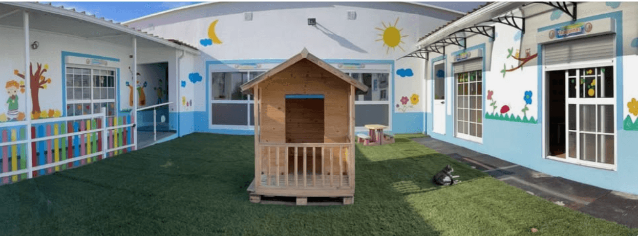 Espaço exterior do Cantinho dos Sonhos, com casinha de madeira, relva e murais coloridos
